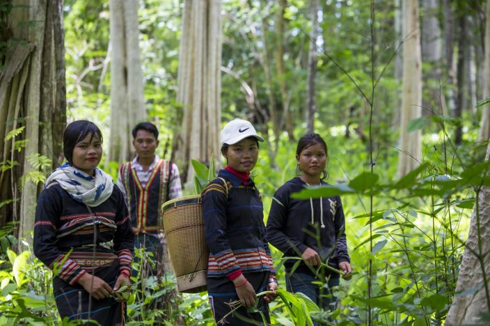 Sav Leat stands behind the young women in the community forest of Pa Tang village while they are posting for a picture to share on their facebook. Photo by Savann Oeurm/Oxfam