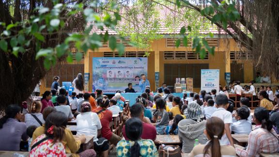 Community members, including parents, teachers, and students, gather under a large shade tree to participate in the FOWASH clean water campaign. Photo: Oxfam 