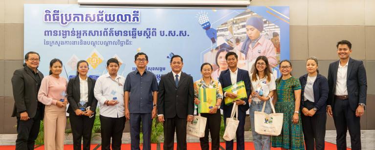 Group photo of six “NSSF Best Reporter Awards” winners with H.E. Dr. Sophannarith Heng, Deputy Director of the National Social Security Fund (center), Ms. Sophoan Phean, Oxfam National Director (green dress), representatives from Oxfam & partner organizations.