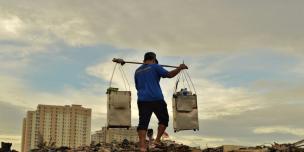 Seorang pedagang bakso pikul keliling berjalan melintasi area yang penduduknya baru saja digusur untuk wilayah pembangunan baru, dekat dengan apartemen mewah di Jakarta Utara, Indonesia. Credit Foto:Tiara Audina/Antropologi UI