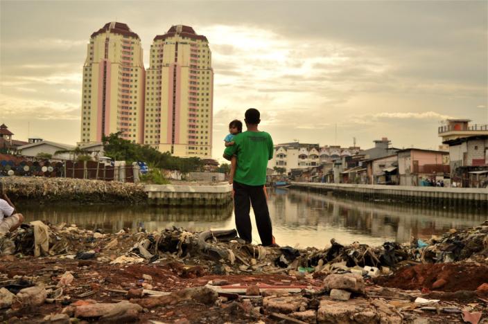 Menatap masa depan: seorang ayah menggendong anak perempuannya ketika berdiri di satu area dimana warga setempat baru saja digusur untuk area pembangunan baru, dekat dengan apartemen mewah di Jakarta Utara, Indonesia. Dalam dua dekade terakhir, ketimpangan antara kelompok orang terkaya dan kelompok lainnya di Indonesia makin meningkat secara lebih cepat ketimbang negara lain di Asia Tenggara. Foto: Tiara Audina/Antropologi UI