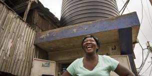 Clarice Akinyi, 35, Domestic Worker by a water tank in Mathare Ward, Mashimoni Village, Nairobi, Kenya. Photo Credit: Katie G. Nelson/Oxfam