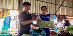 A student from the National University of Laos hand a bamboo basket to a wet market vendor