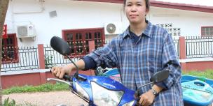 A lao woman standing next to a motorbike she used to deliver food to her customers during the pandemic