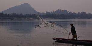 A fisherman casts his net into the river