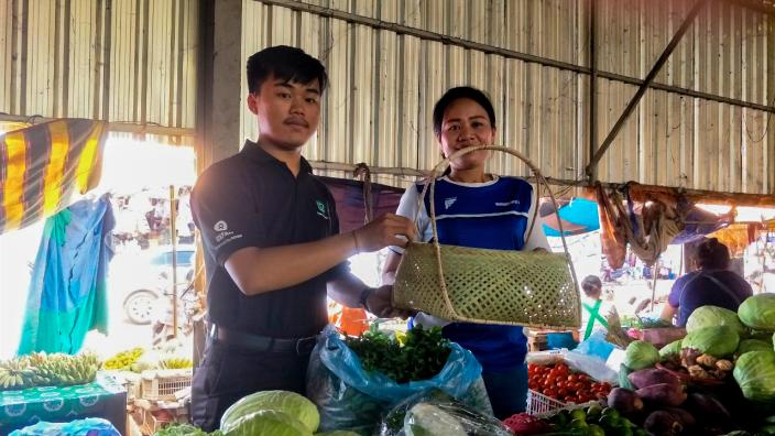 A student from the National University of Laos hand a bamboo basket to a wet market vendor
