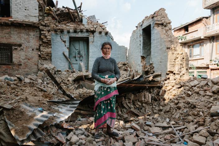 An earthquake survivors stands by her collapsed house - Credit: Aubrey Wade/Oxfam