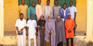 A group of community volunteer teachers standing together outside a school building in Kwaya Kusar.