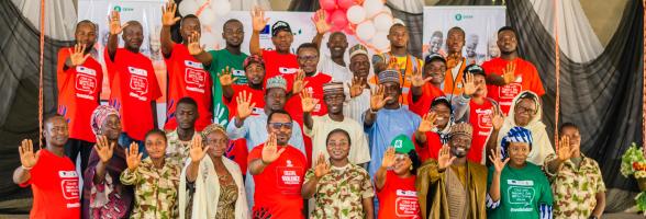 Group of 25+ participants in orange and green shirts raising hands, symbolizing a collective commitment to end GBV at an Oxfam event in Biu