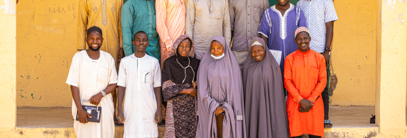 A group of community volunteer teachers standing together outside a school building in Kwaya Kusar.
