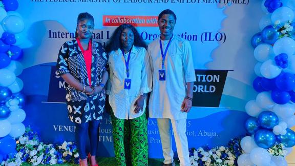 Three members of the Oxfam team standing in front of the event banner at the policy re-validation meeting.