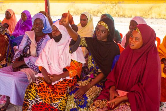 A young woman raising her hand to speak during an interactive community dialogue on women's rights and economic empowerment in Kwaya Kusar, North East Nigeria.