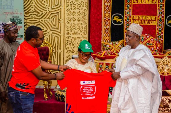 Advocacy team inaugurating a traditional leader (Emir of Biu) as a Gender Champion, presenting an Orange T-shirt with the text "Say NO to Online Abuse."