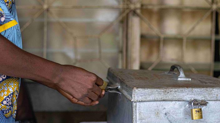 A close-up shot of a person's hand using a key to unlock a metal savings box, highlighting the secure nature of the Village Savings and Loan Association (VSLA) model.