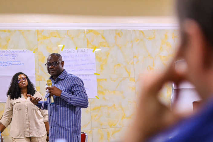 Country Director Hamza Ahmed Tijani speaks passionately into a microphone while gesturing with his hand during the 'CONTEXT CHECK-IN' session.