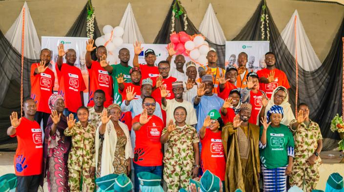 Group of 25+ participants in orange and green shirts raising hands, symbolizing a collective commitment to end GBV at an Oxfam event in Biu