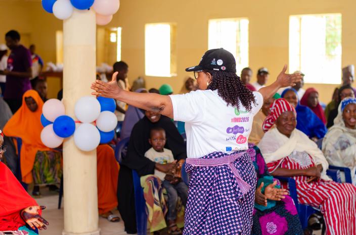 A passionate female leader with her arms wide open engaging a joyful audience of women and children during the Biu LGA empowerment dialogue.