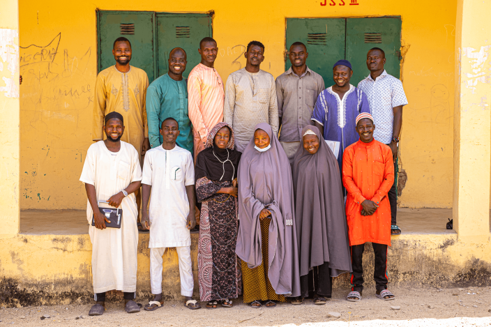 A group of community volunteer teachers standing together outside a school building in Kwaya Kusar.