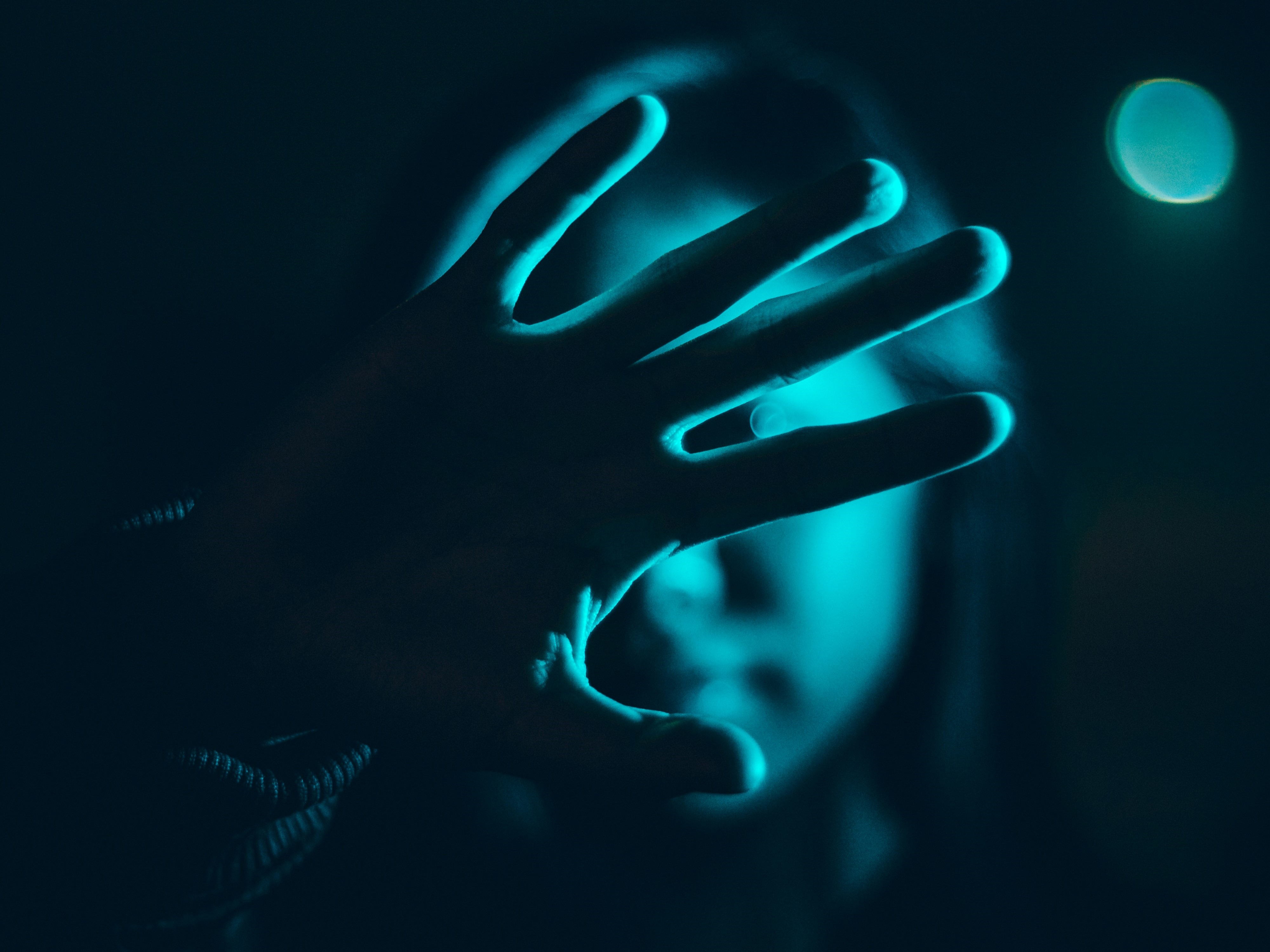 A woman holding her hand up against teal-blue light in a dark setting.