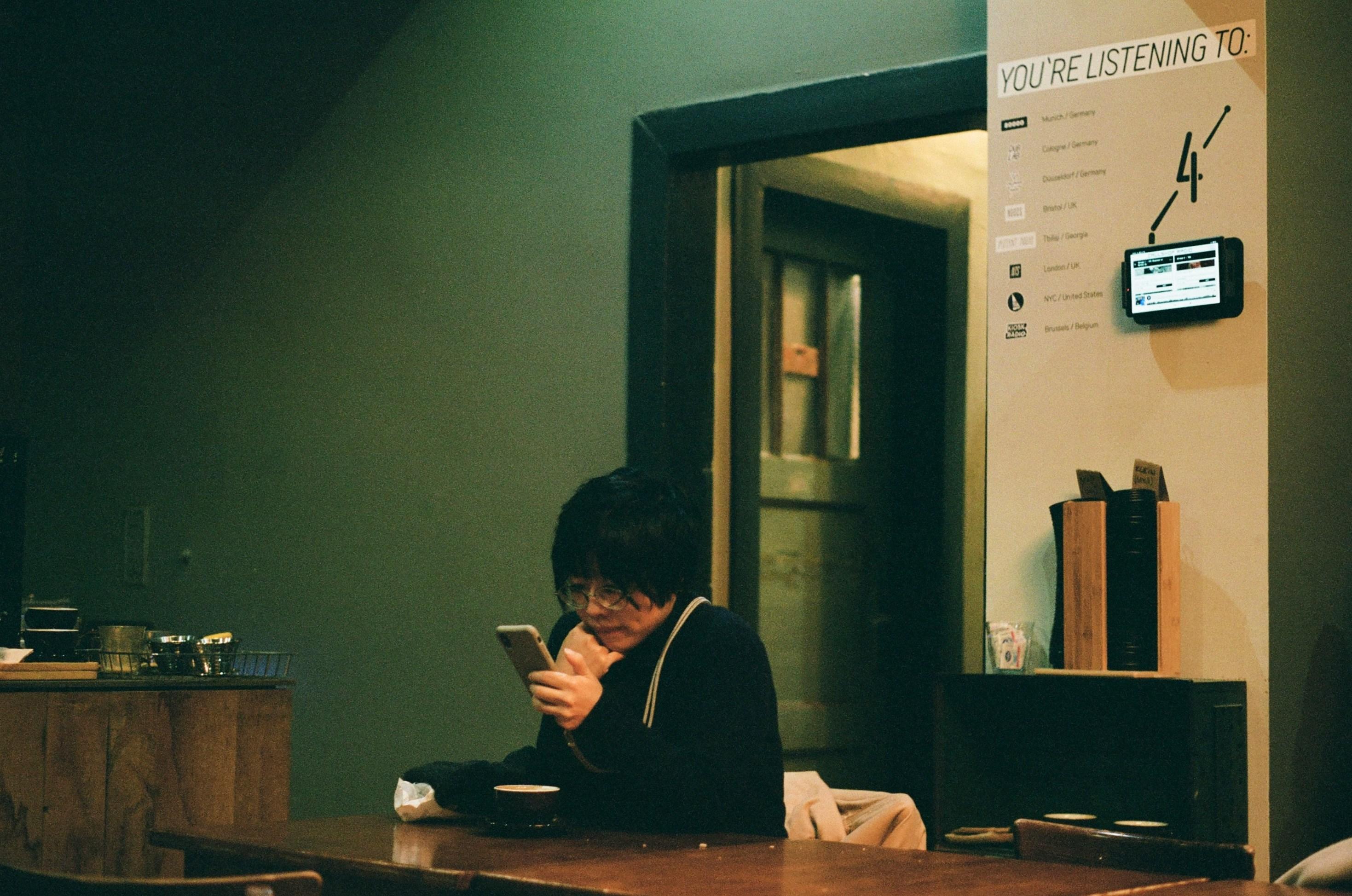 Photo of a woman sitting at a table looking at a smartphone.