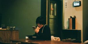Photo of a woman sitting at a table looking at a smartphone.