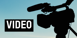 Silhouette of a professional video camera mounted on a tripod against a clear blue sky. Text reading "video".