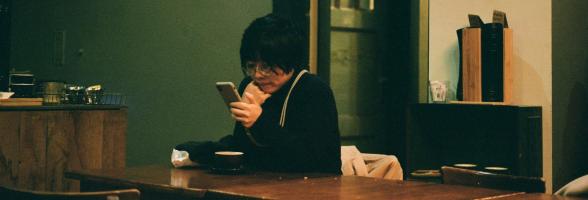 Photo of a woman sitting at a table looking at a smartphone.