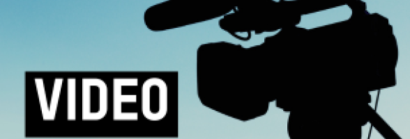 Silhouette of a professional video camera mounted on a tripod against a clear blue sky. Text reading "video".