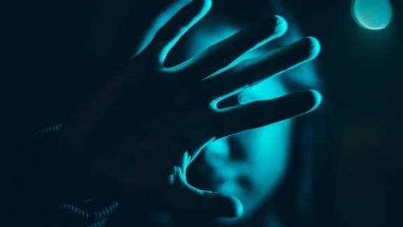 A woman holding her hand up against teal-blue light in a dark setting.