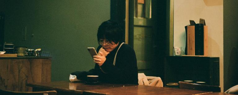 Photo of a woman sitting at a table looking at a smartphone.