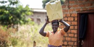 Alur Florence fetches water as her husband does other chores at home. photo credit Julius Kasujja/Oxfam