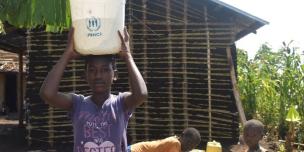 Sarah carrying a bucket of water on her head after fetching it from the new water source in Kyaka II refugee settlement.
