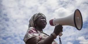 Sarah, the chairperson of a handicrafts group in Bidibidi refugee setttlement, uses a microphone to call women to join her group. Photo: Kieran Doherty/Oxfam