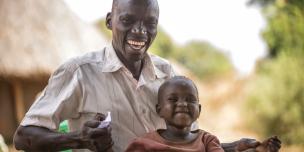 David Zakayo with his child. Through the Oxfam We care training, men like David now help out in house hold chores as well as taking care of their children. Most men in David's community in Lamwo district would leave all the responsibility of care work to women