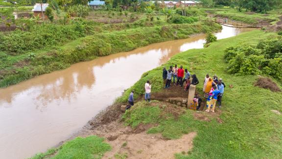 Moses poses with community members beside the river gauge, symbolizing collective preparedness.