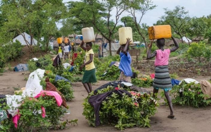 At the Bidi Bidi refugee settlement in Uganda, women carry water back to their shelters. The settlement is now home to more than 287,000 refugees. Photo by Coco McCabe/Oxfam